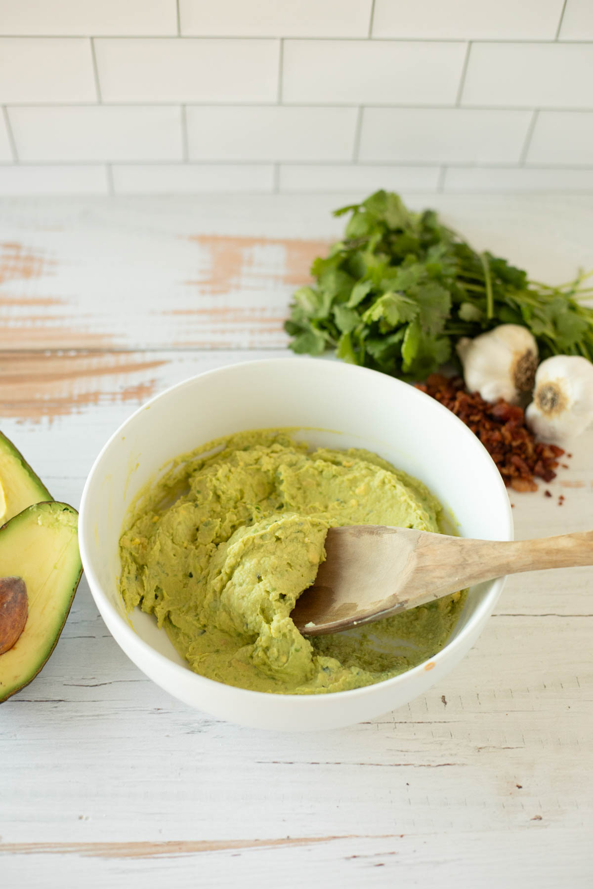 A bowl of freshly made avocado mixture with a wooden spoon on a kitchen counter.