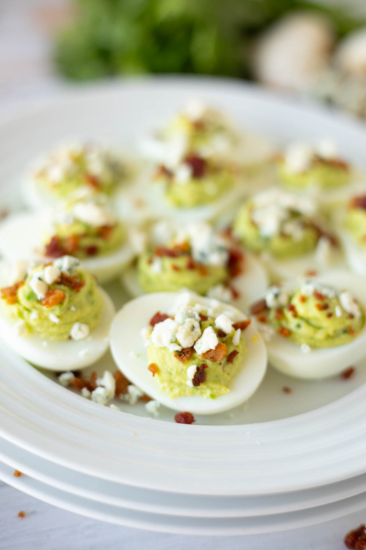 A plate of deviled eggs garnished with bacon and crumbled cheese.