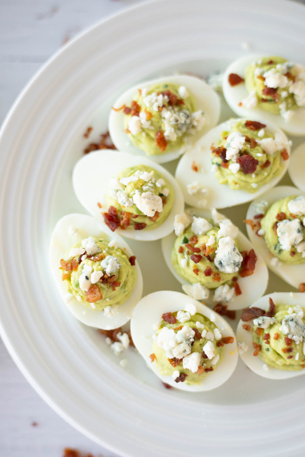 A plate of deviled eggs topped with crumbled bacon and blue cheese.