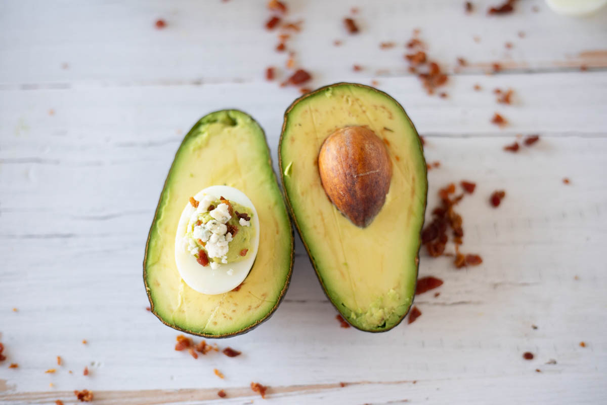 Halved avocado with seed visible and topped with feta cheese on a wooden surface.