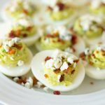 A plate of deviled eggs topped with blue cheese and bacon bits.