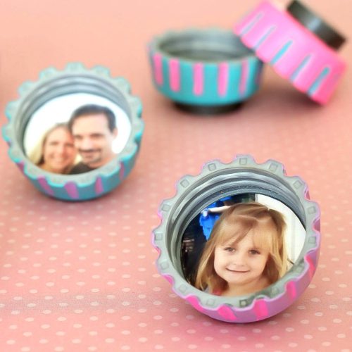 Three custom bottle caps with photos inside on a pink dotted surface; one cap shows a couple, another a young girl, with a blue focus on the girl's cap.