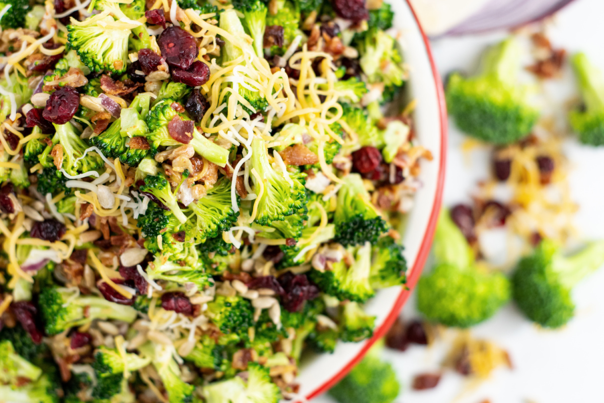 Close-up of a broccoli salad with dried cranberries, sunflower seeds, and shredded cheese.