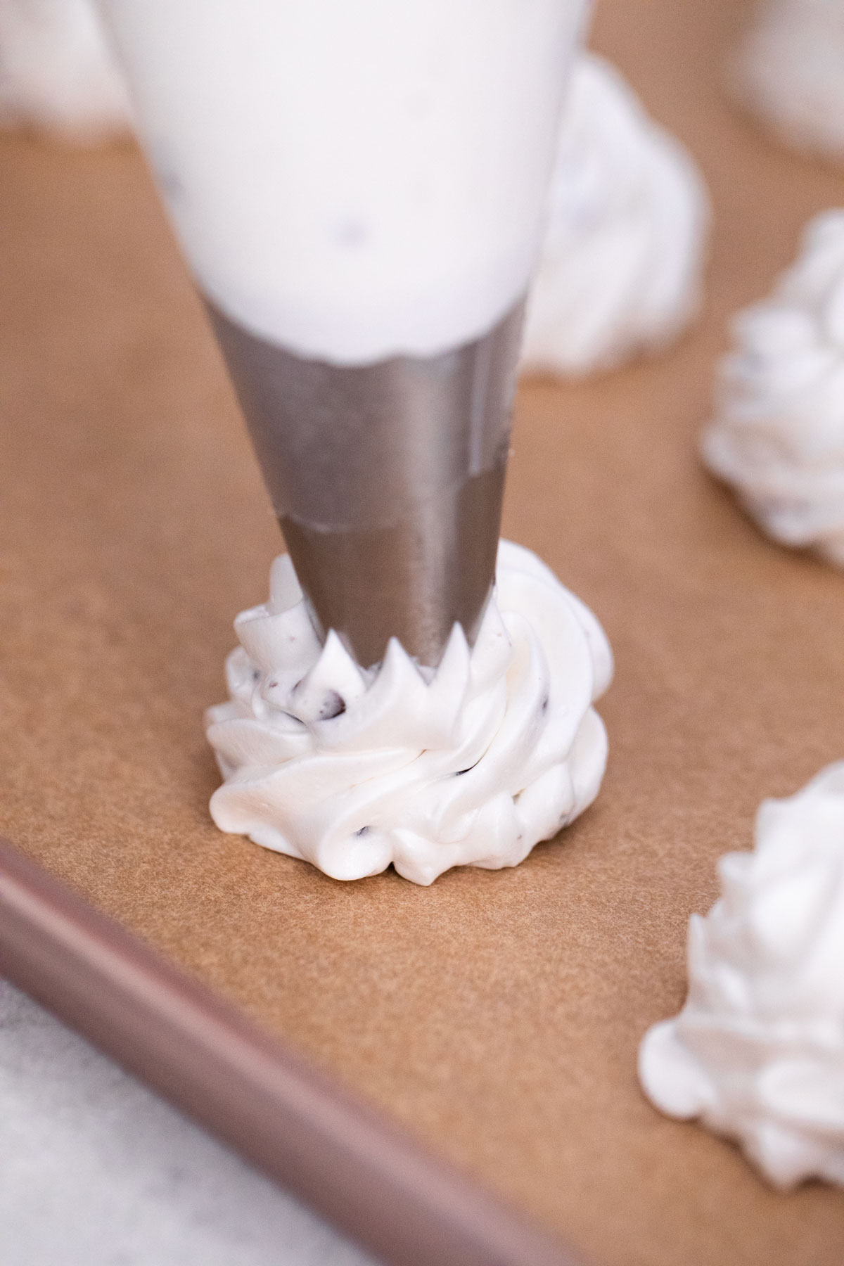 A pastry bag with a metal tip piping meringue onto parchment paper, forming a swirl next to other completed swirls.