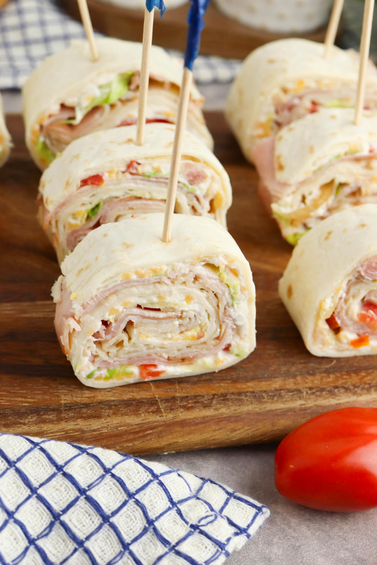 Turkey and cheese wraps with lettuce and tomatoes on a wooden cutting board, secured with toothpicks.