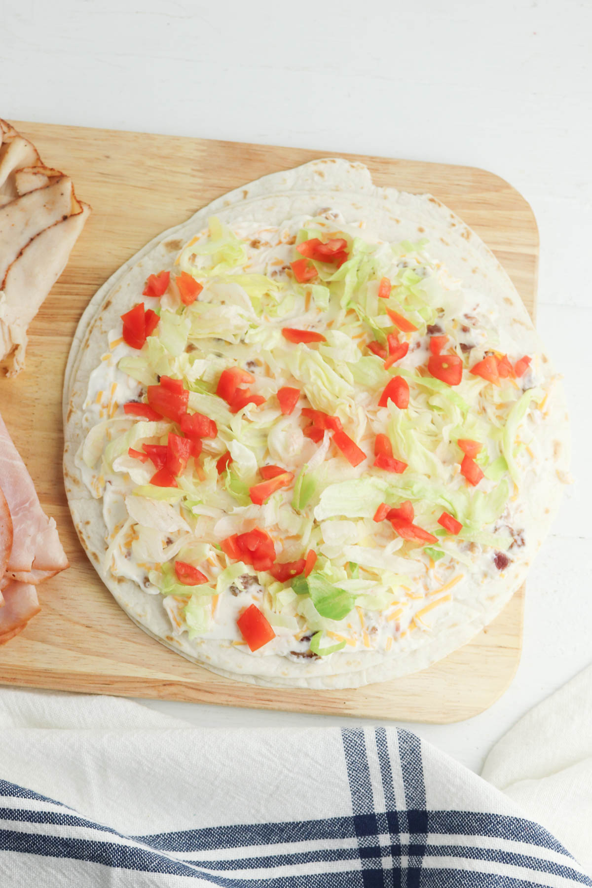 A flour tortilla on a wooden cutting board topped with shredded lettuce and diced tomatoes