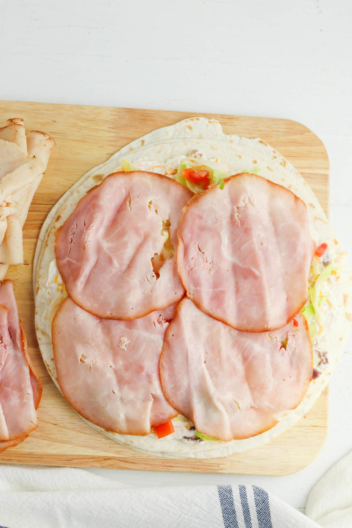 Open-faced tortilla with ham slices on a wooden cutting board.
