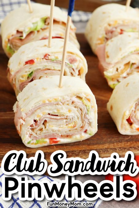 Club sandwich pinwheels on a wooden board, featuring rolled tortillas with layers of meats, cheeses, and veggies, secured with toothpicks.
