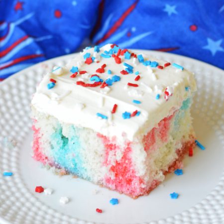 A colorful piece of frosted cake with red, white, and blue layers and sprinkles on a white plate.
