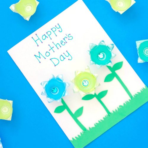 Handmade mother's day card with "happy mother's day" text, decorated with blue and yellow paper flowers with button centers, on a bright blue background.