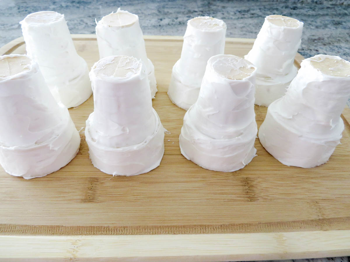 Several small, white frosted ice cream cones on a wooden board
