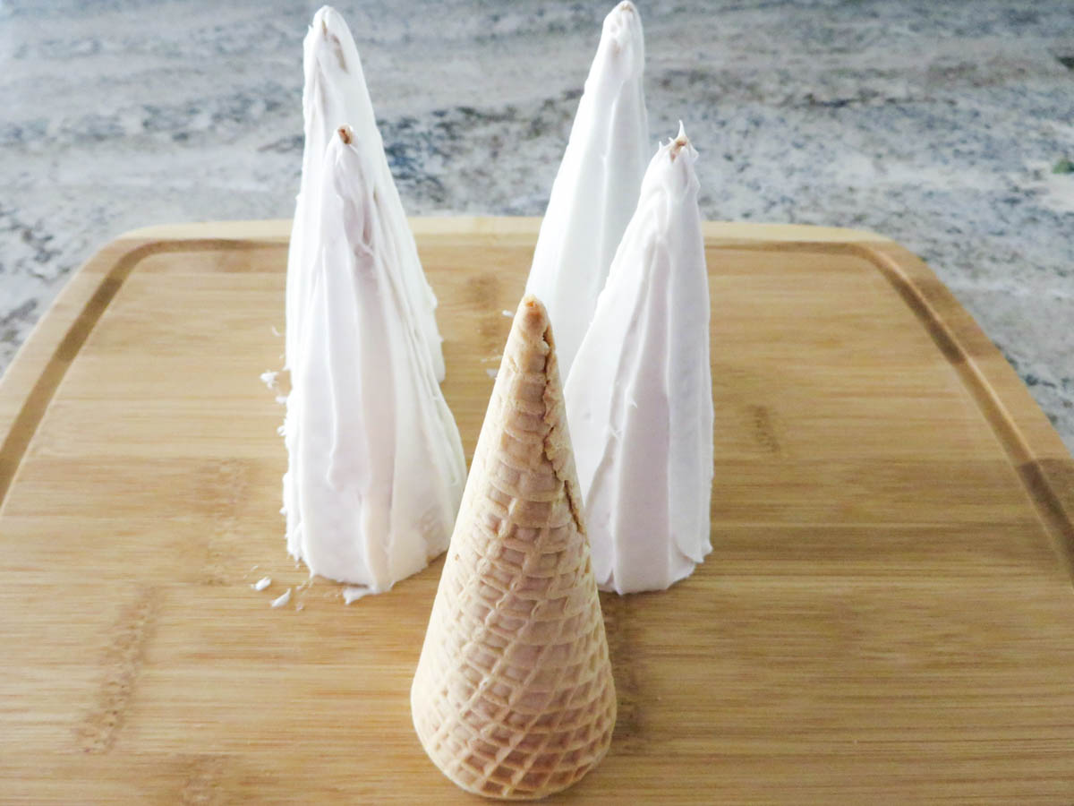 Five ice cream cones on a wooden board, with four frosted and one unfrosted.