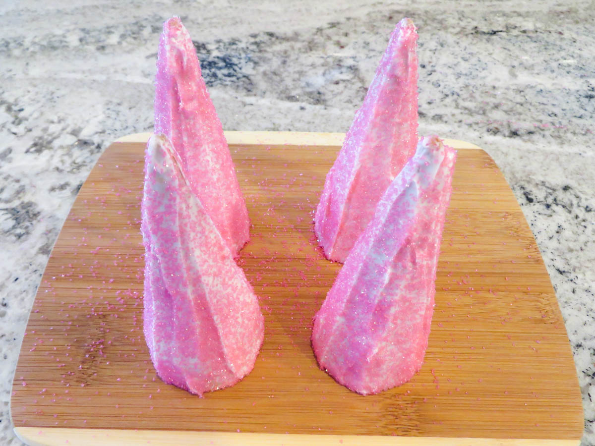 Three pink sugar-coated candies shaped like cones on a wooden cutting board.