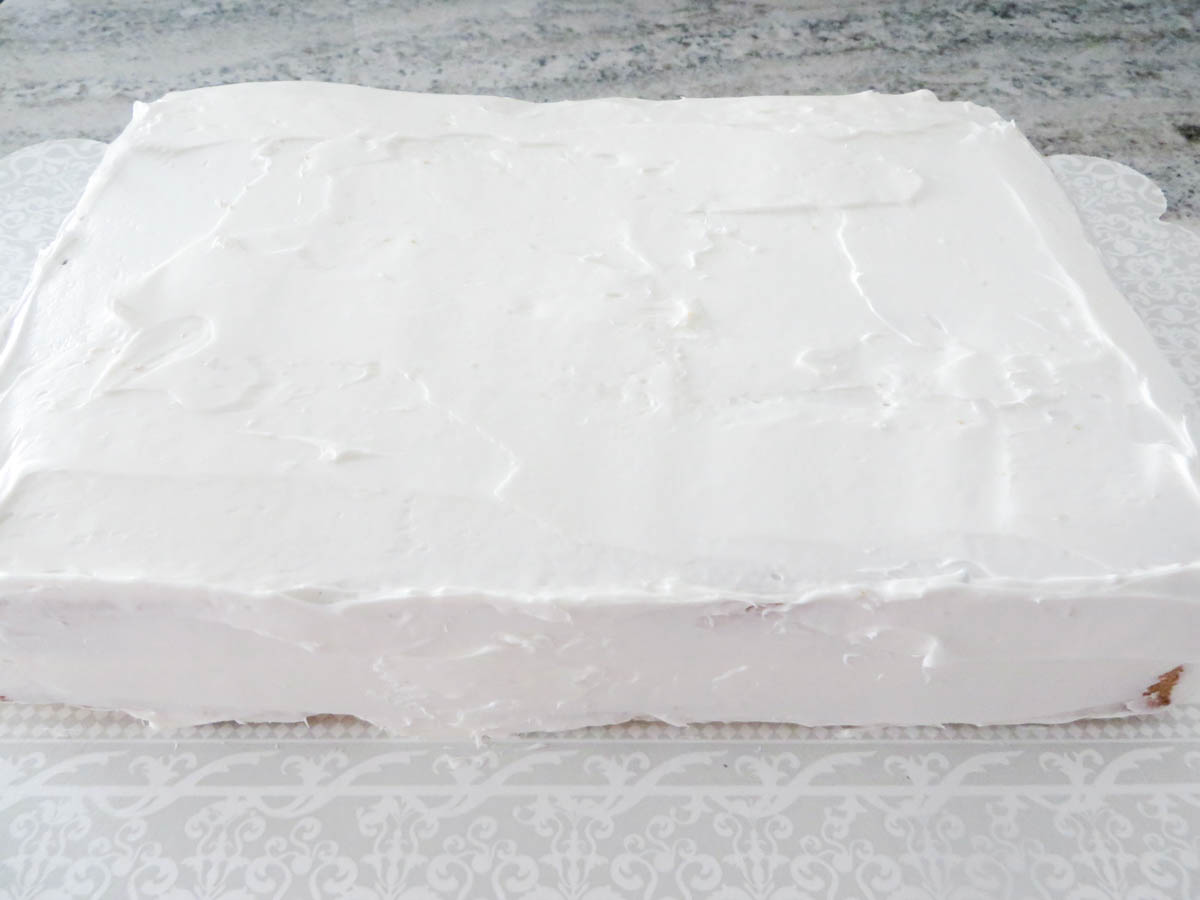 A large rectangular cake with white frosting on a floral patterned board