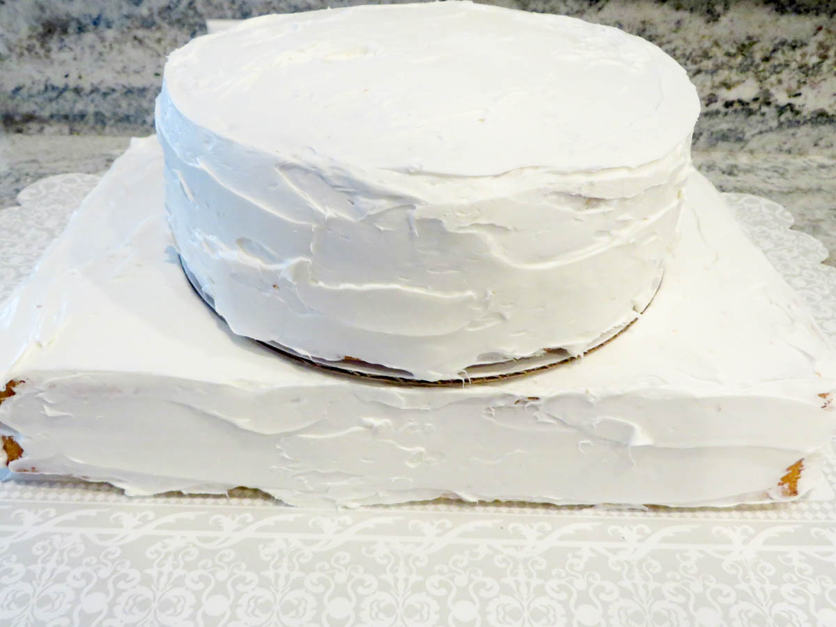 A homemade two-layer cake with white icing on a silver tray, set upon a lace-patterned tablecloth.