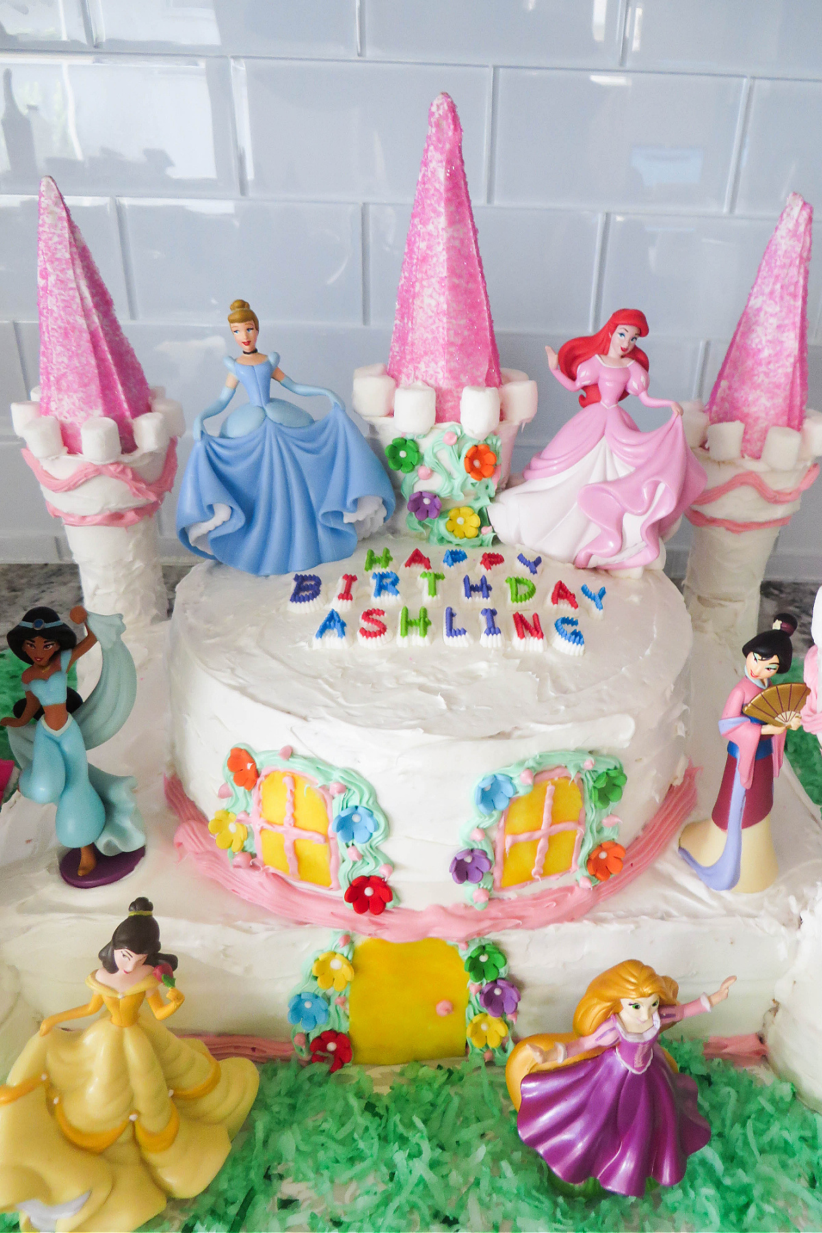 A colorful princess-themed birthday cake with figurines of disney princesses and pink castle turrets