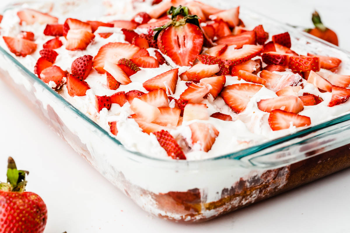 A glass baking dish with a strawberry dessert layered with whipped cream and fresh strawberry slices.