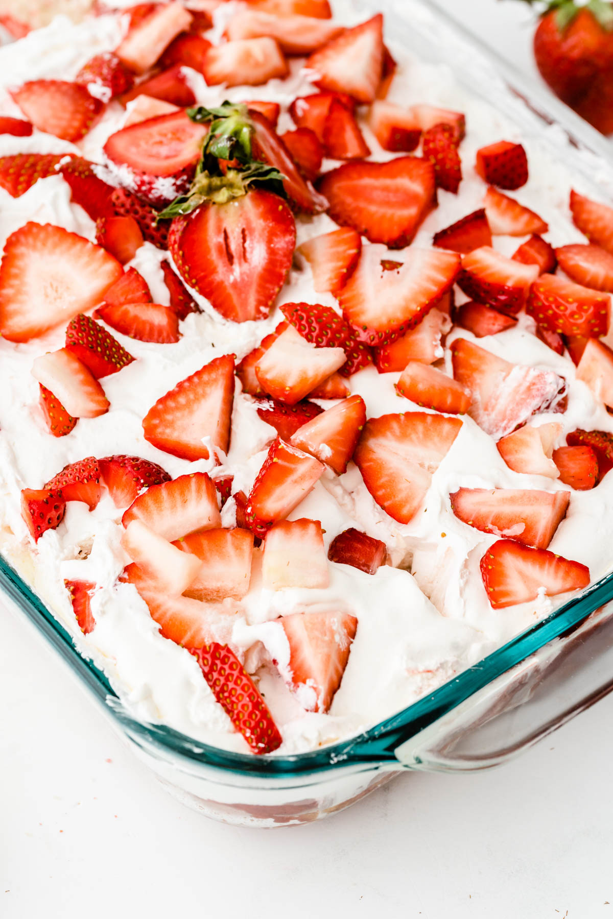 A glass dish filled with a dessert topped with whipped cream and fresh strawberry slices.