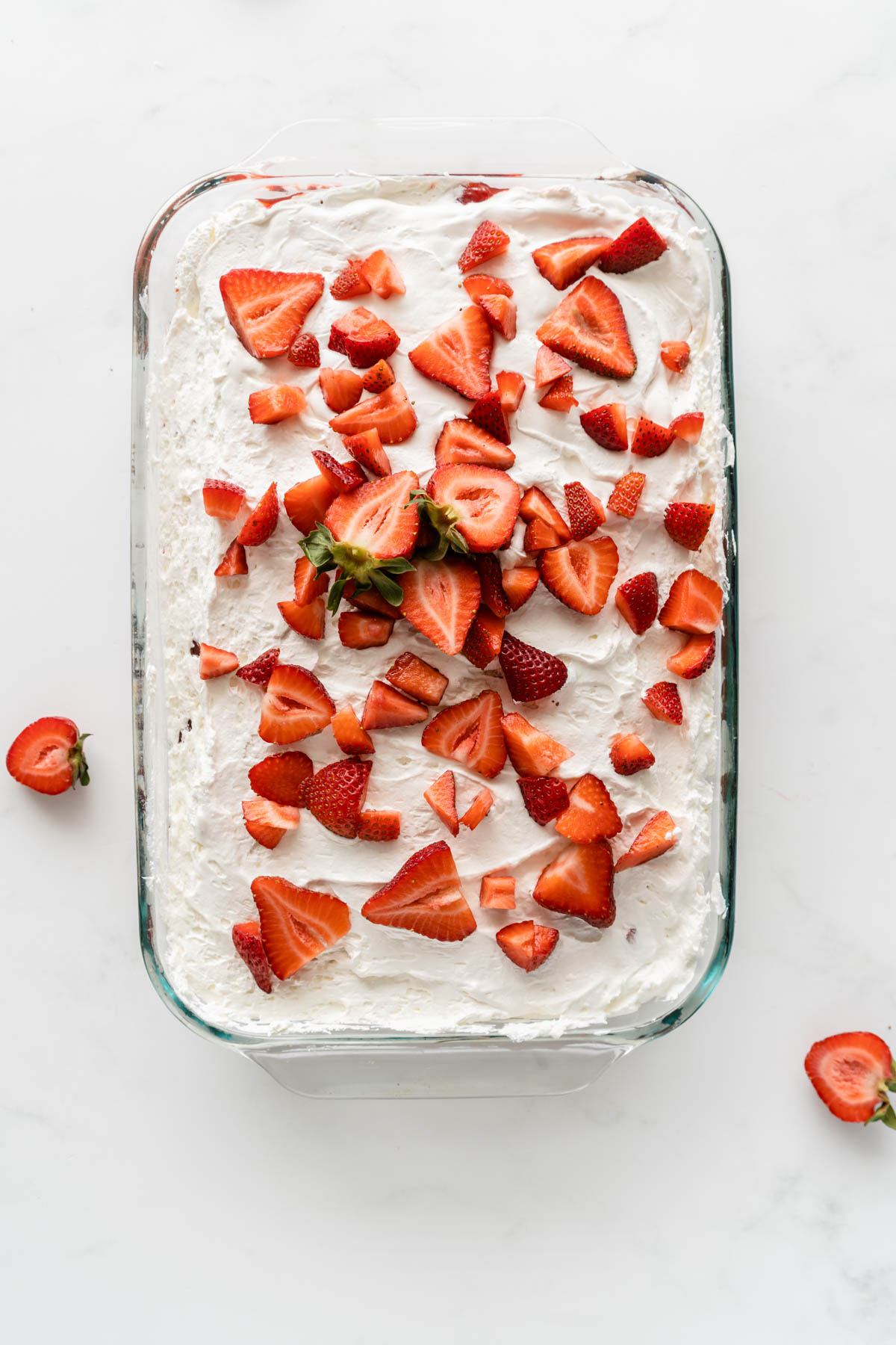 A glass dish of dessert topped with whipped cream and fresh sliced strawberries.