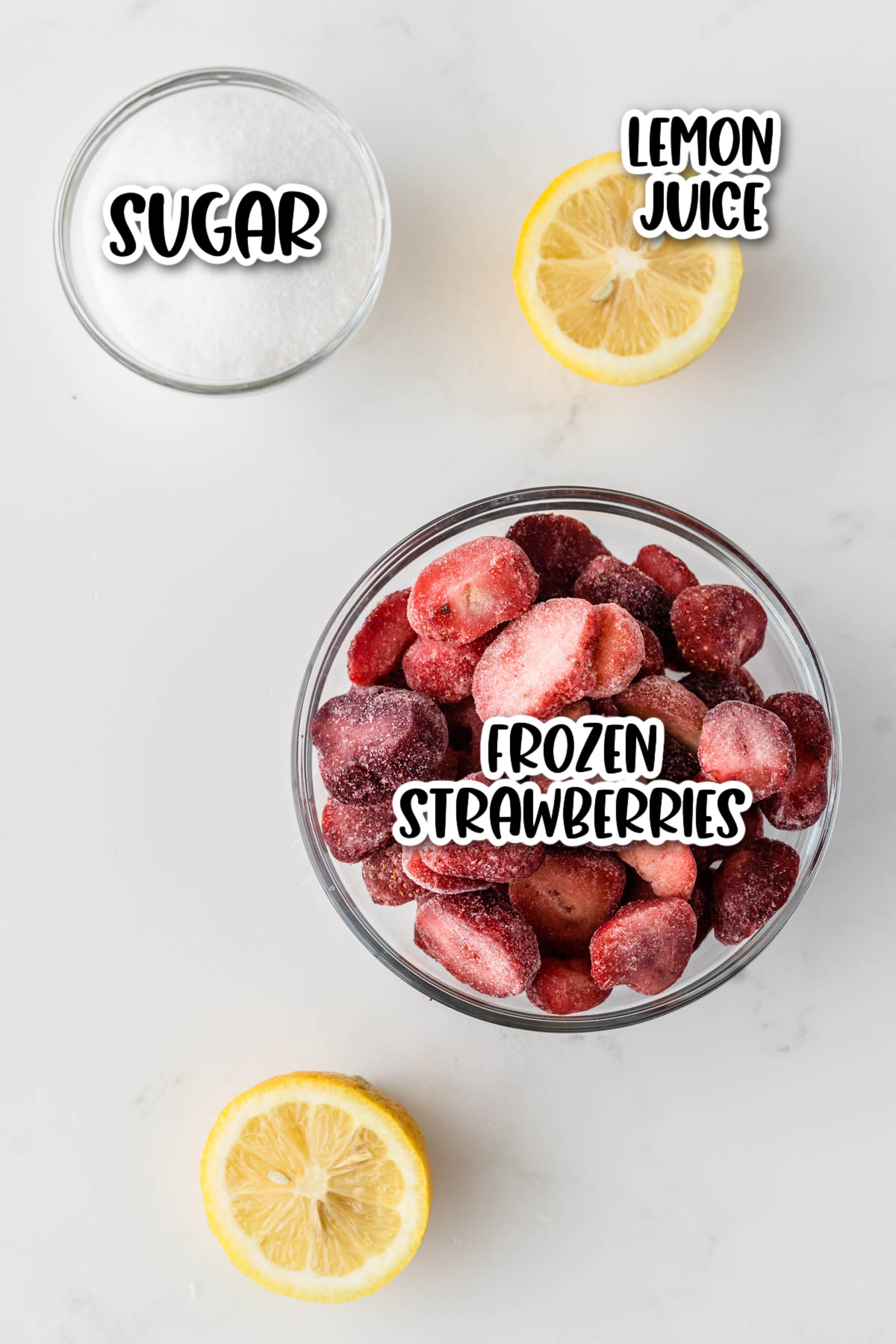 A bowl of frozen strawberries with containers of sugar and lemon juice labeled, arranged on a marble surface.