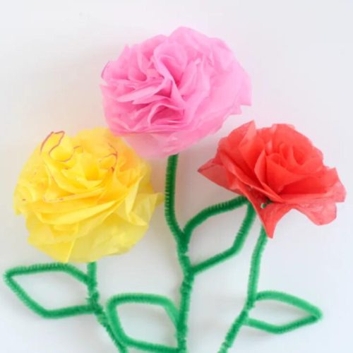 Three colorful tissue paper flowers—pink, yellow, and orange—with green pipe cleaner stems on a white background.