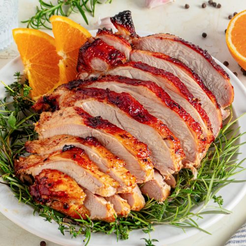 Sliced roasted turkey breast on a plate garnished with fresh herbs and orange slices.