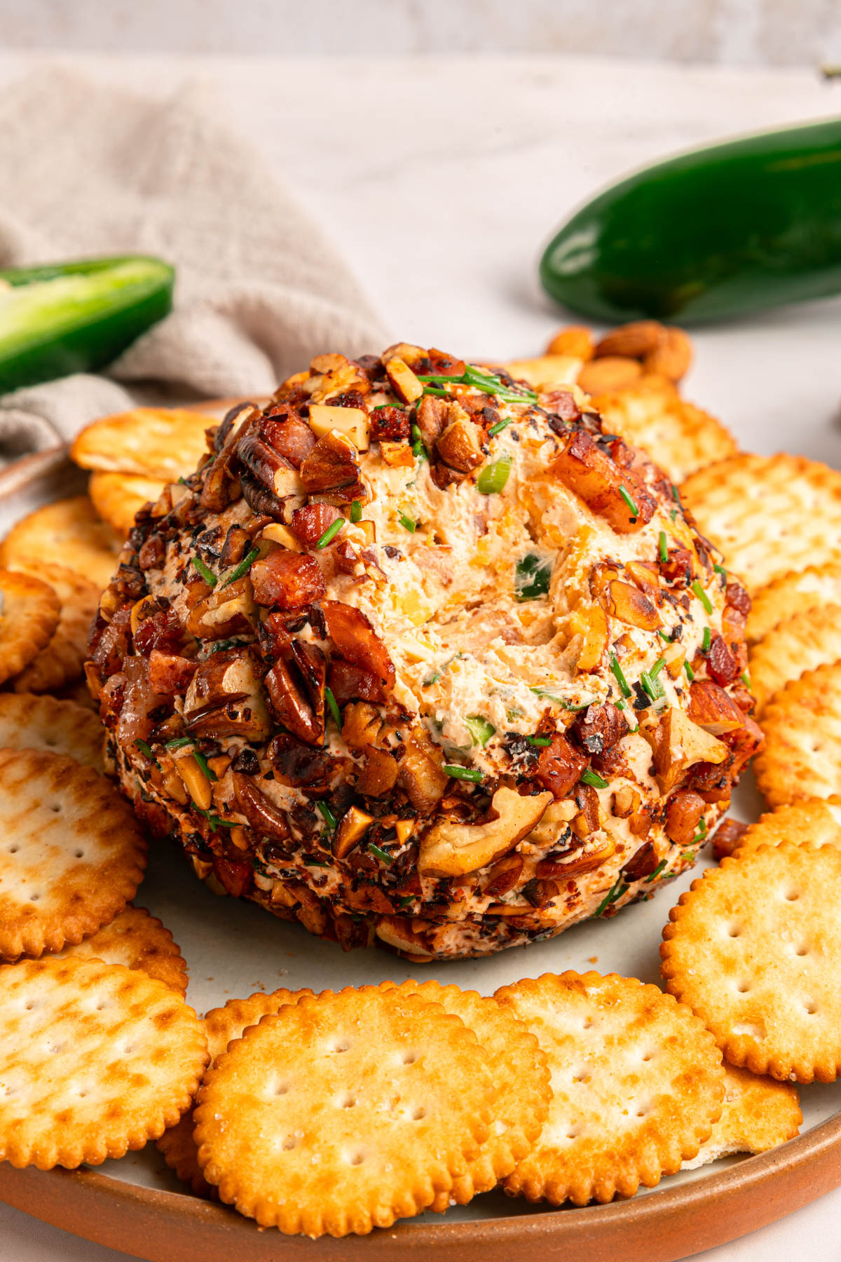 A cheese ball coated with nuts and herbs is served on a plate surrounded by round crackers.