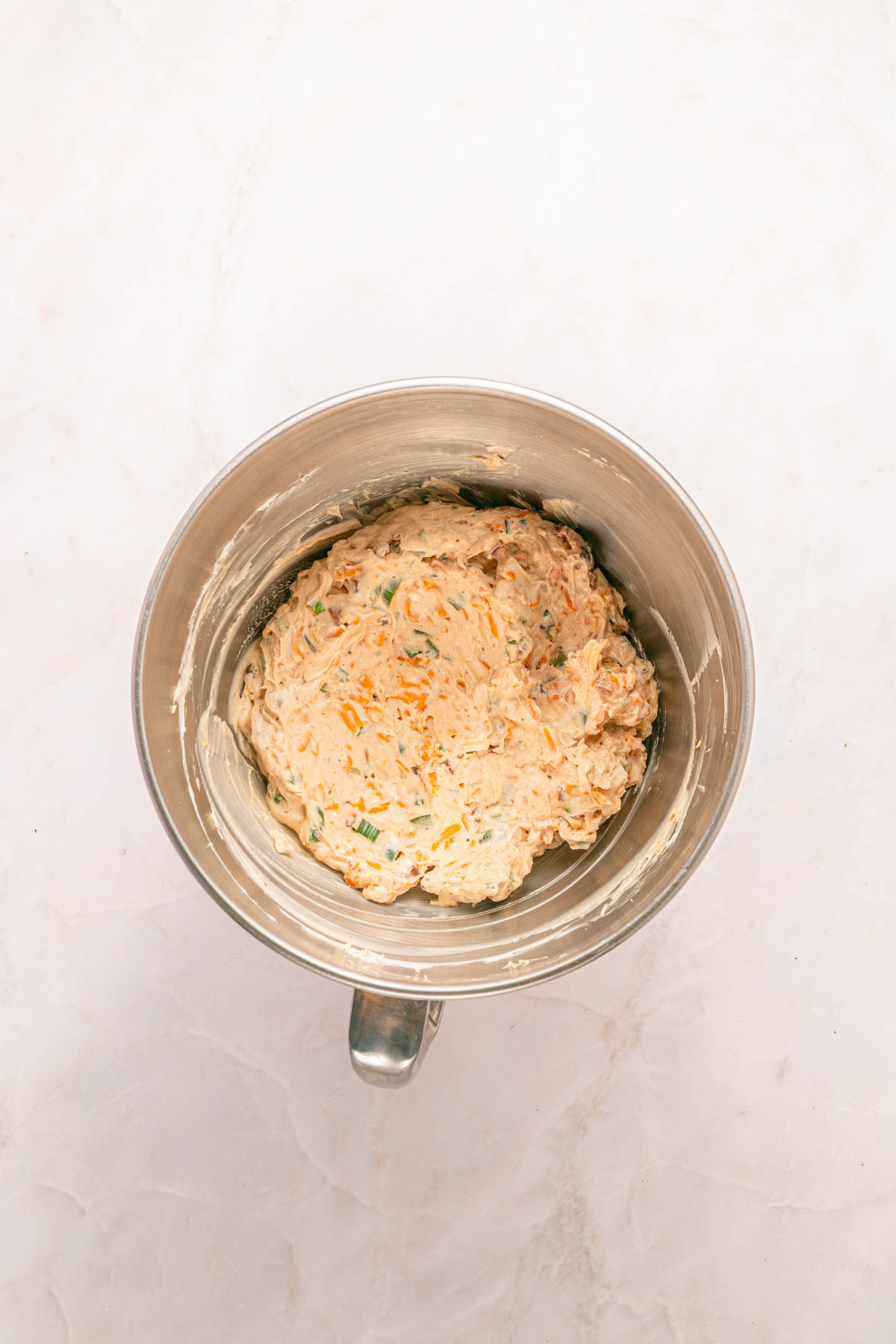 A metal mixing bowl containing cream cheese, cheese and green onion mixture. 