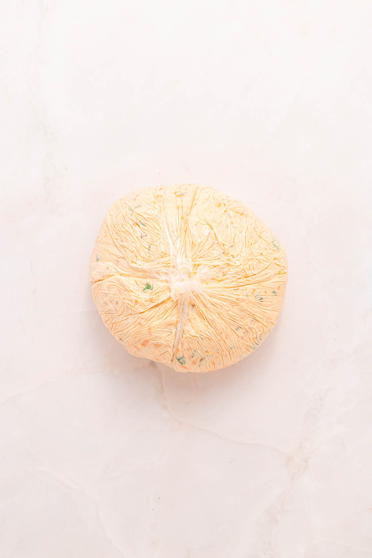 Cheese ball mixture wrapped tightly in a ball with plastic wrap. 