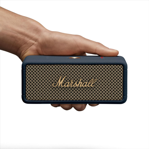 A hand holds a navy blue Marshall portable Bluetooth speaker with a gold mesh grille and the Marshall logo on the front.