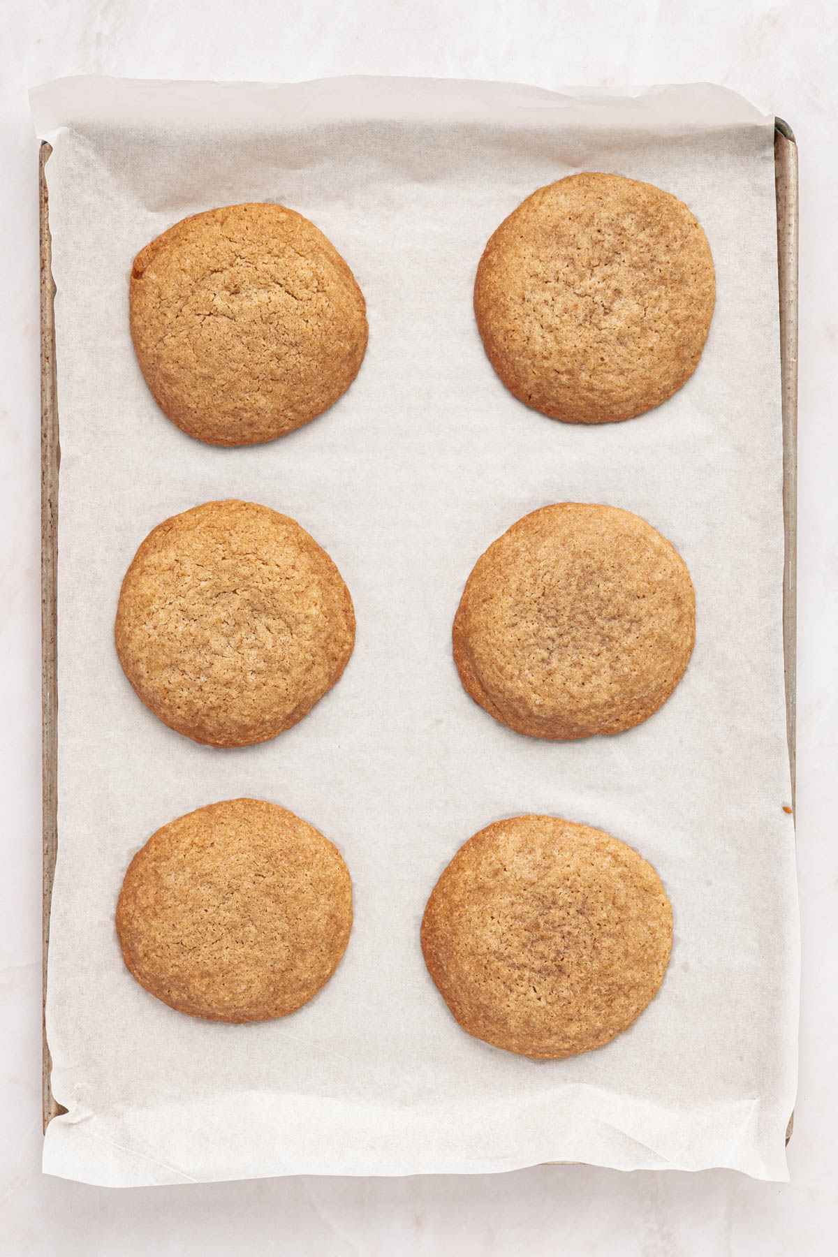 Six round cookies are evenly spaced on a parchment-lined baking sheet.