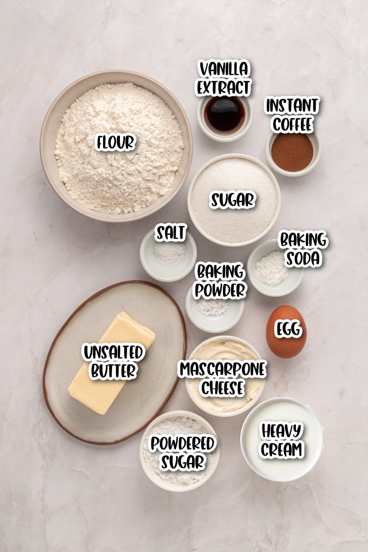 Assorted baking ingredients in bowls and plates labeled: flour, sugar, salt, baking powder, baking soda, instant coffee, vanilla extract, egg, unsalted butter, mascarpone cheese, powdered sugar, heavy cream.