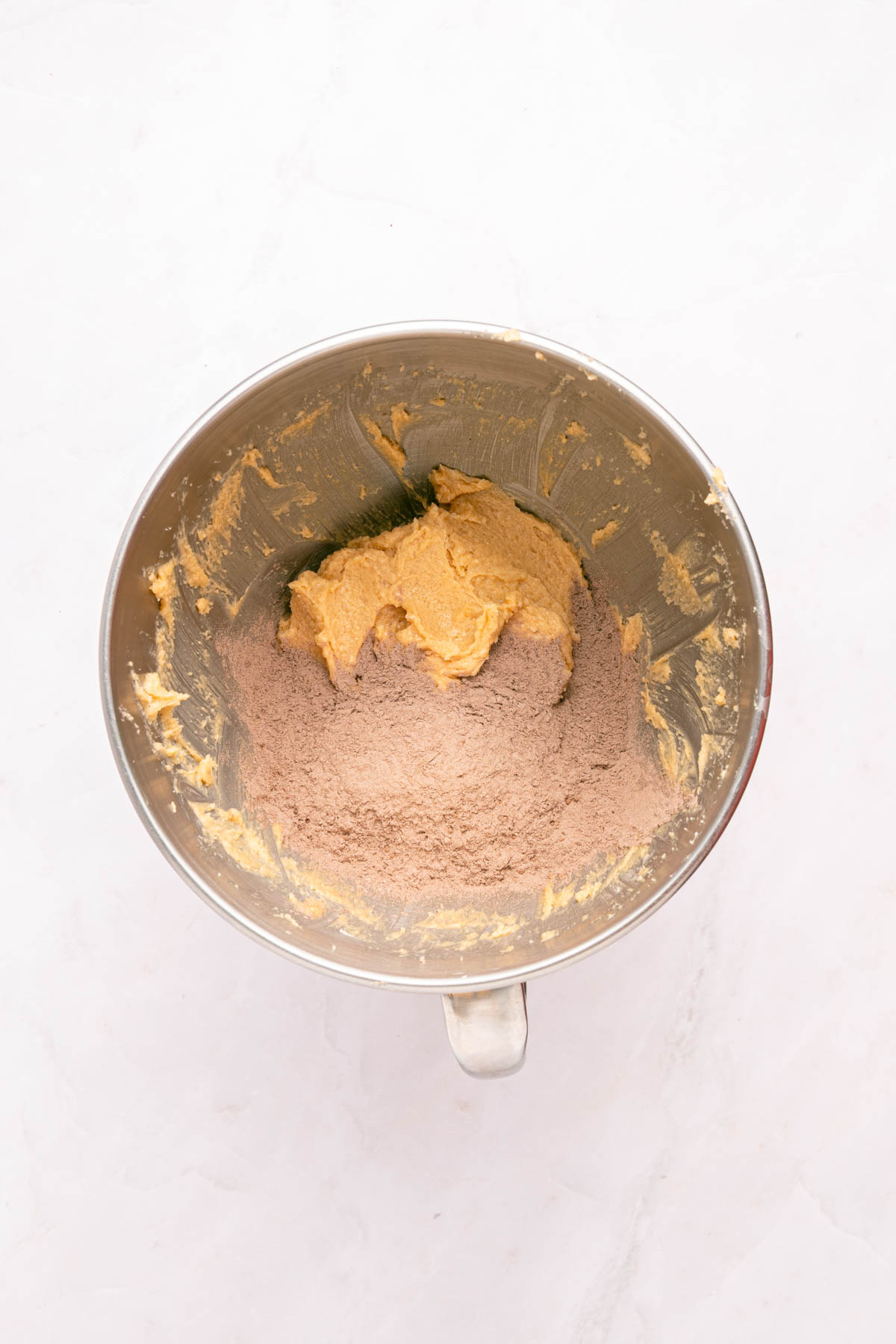 A mixing bowl containing partially blended cookie dough with dry cocoa powder and wet ingredients.