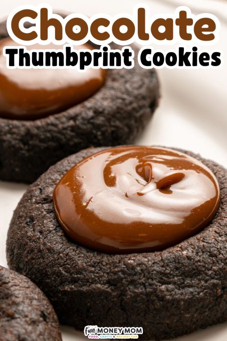 Close-up of chocolate thumbprint cookies topped with glossy chocolate filling, arranged on a light surface. Text overlay reads "Chocolate Thumbprint Cookies.
