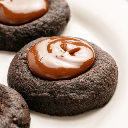 Chocolate thumbprint cookie with a swirl of glossy chocolate filling on a white plate.