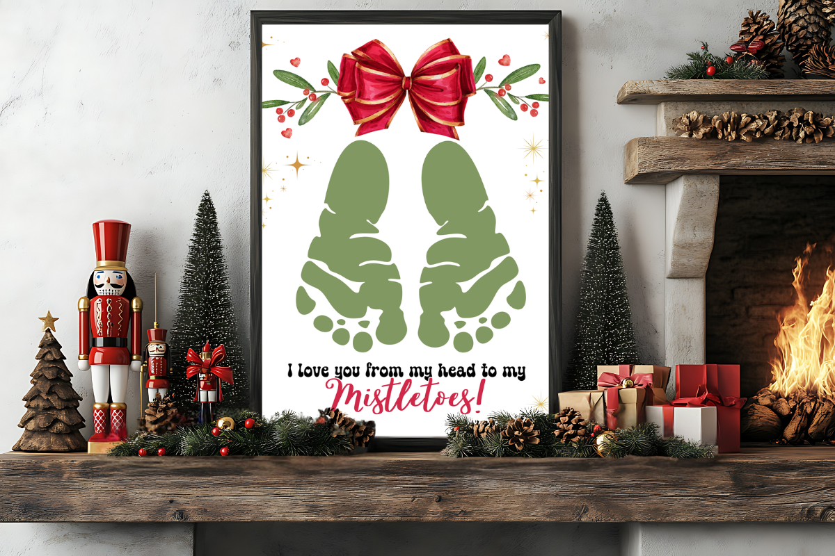 A framed holiday print with green footprints, a red bow, and the text "I love you from my head to my mistletoes!" on a decorated mantel with gifts and nutcracker figurines.