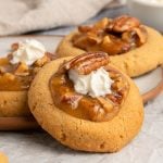 A close-up of cookies topped with caramel, chopped pecans, a dollop of whipped cream, and a whole pecan on a plate.