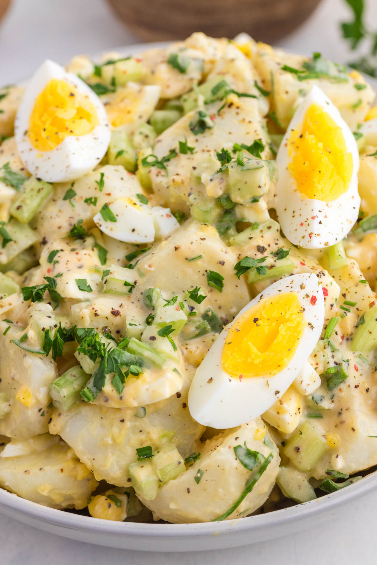 A bowl of potato salad with chopped celery, herbs, and slices of hard-boiled egg on top, all mixed with a creamy dressing.