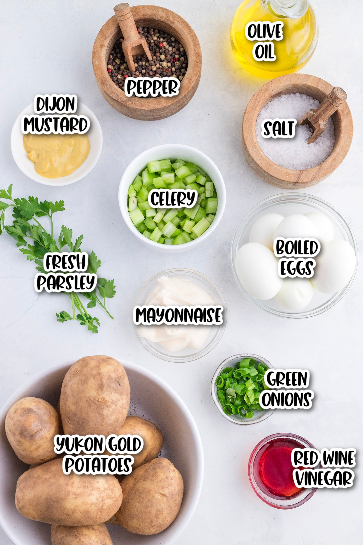 Various potato salad ingredients including Yukon gold potatoes, boiled eggs, celery, green onions, parsley, mayonnaise, Dijon mustard, olive oil, red wine vinegar, salt, and pepper.