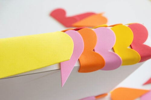Colorful paper hearts in pink, orange, and yellow are arranged along the edge of a white surface.