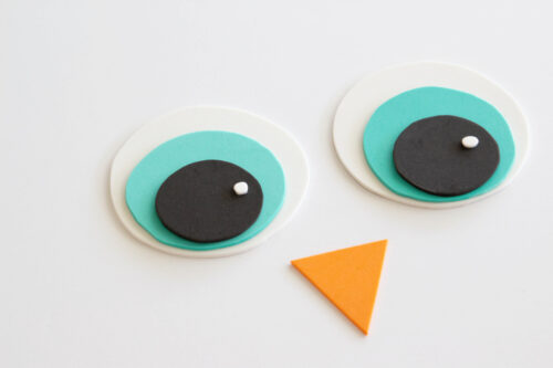 Two layered circular shapes resembling eyes and an orange triangle below them, arranged on a white background to suggest a simple face, possibly of a cartoon bird.