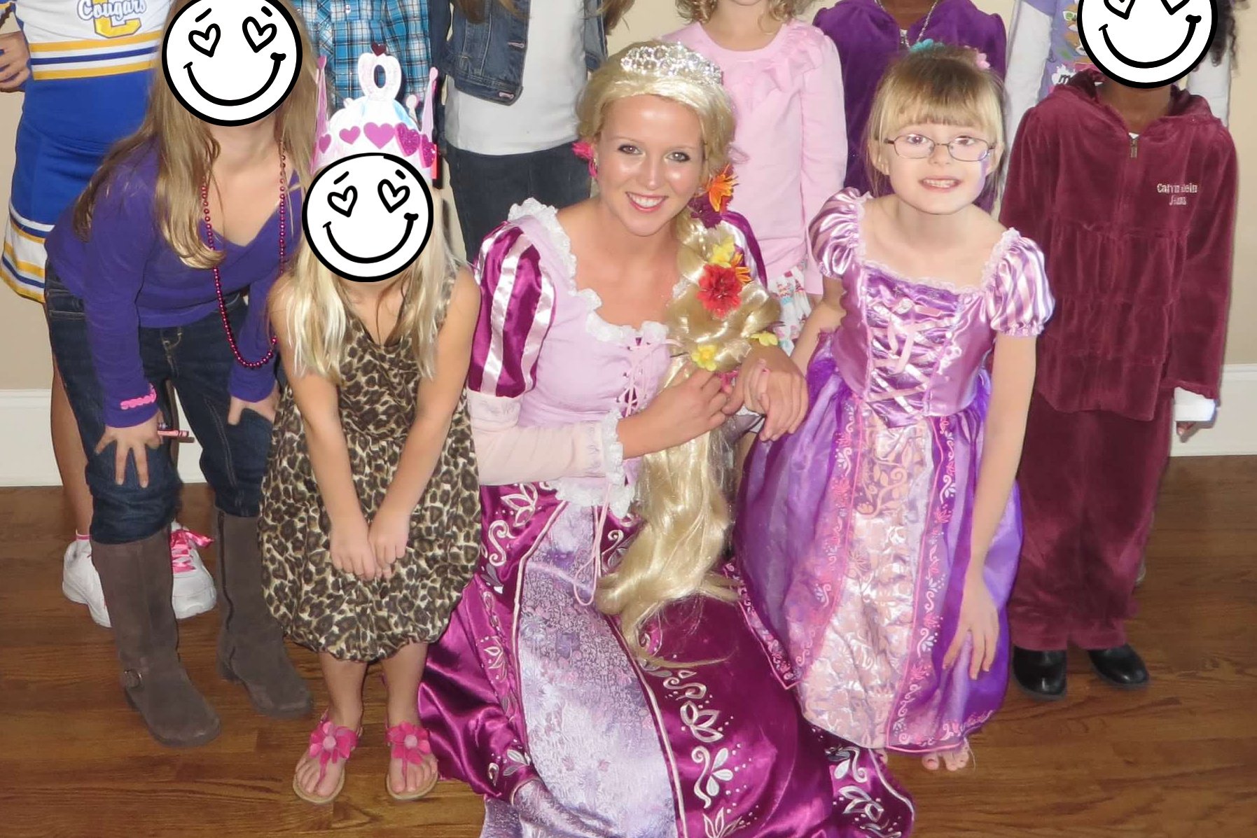A woman dressed as Rapunzel kneels on the floor with children in costumes, including a girl in a purple princess dress, for a group photo indoors.
