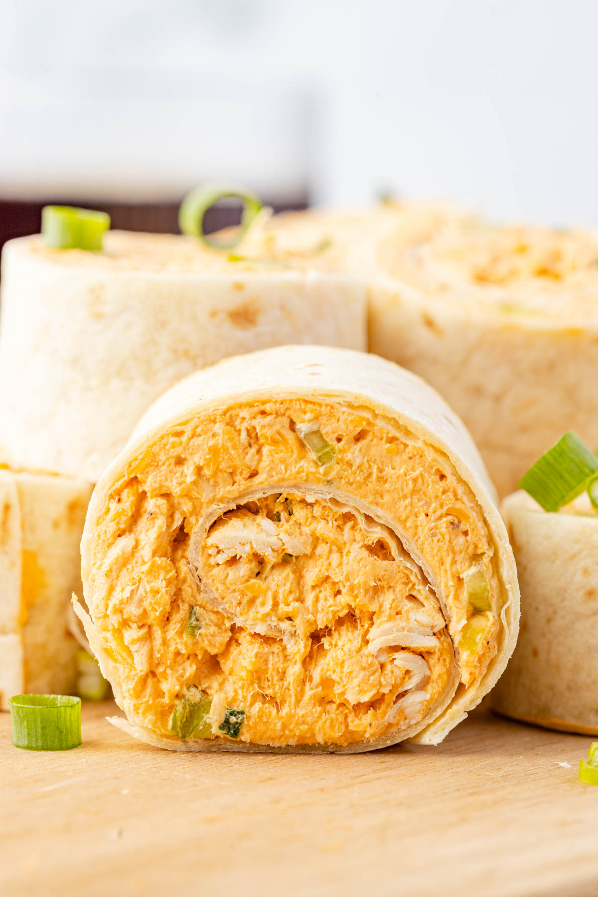 A close-up of sliced tortilla pinwheels filled with a creamy orange chicken mixture, garnished with chopped green onions on a wooden surface.