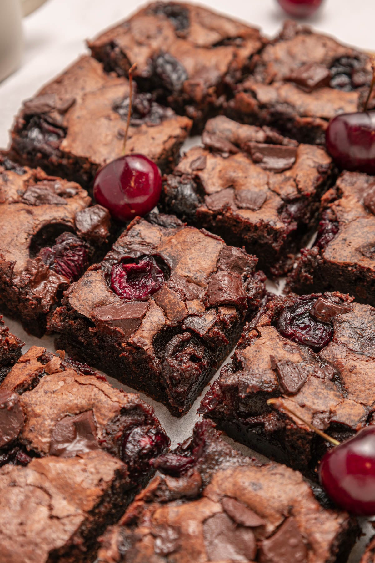 Close-up of chocolate brownies with pieces of cherries on top, cut into squares and arranged closely together.