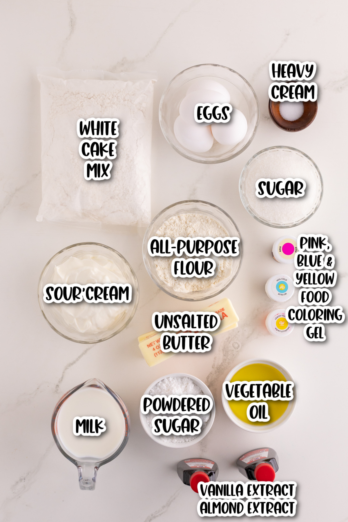 Top-down view of baking ingredients in bowls and containers, including white cake mix, eggs, cream, sugar, flour, sour cream, butter, oil, milk, powdered sugar, extracts, and food coloring gel.