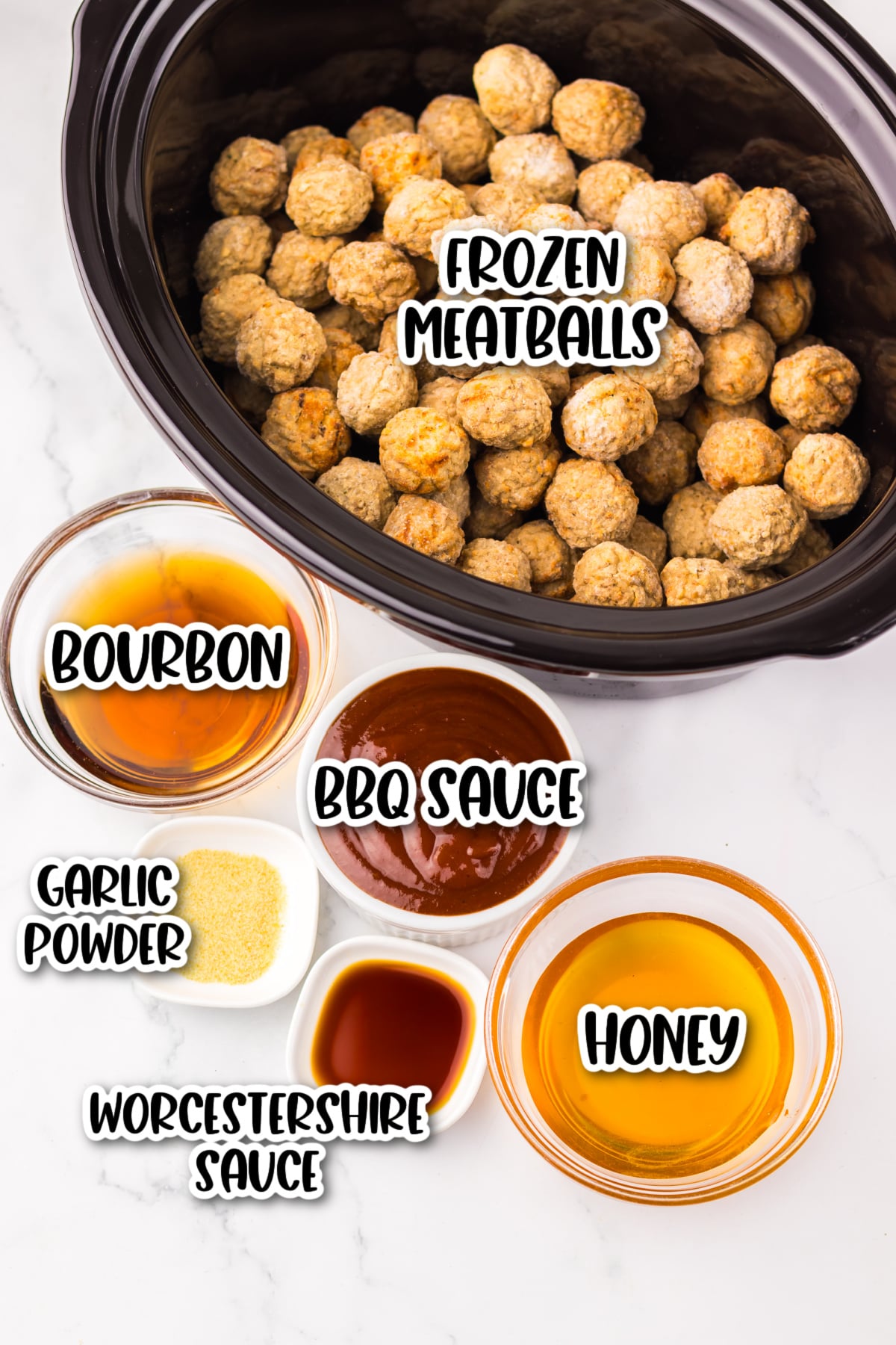 A slow cooker with frozen meatballs, and small bowls of bourbon, BBQ sauce, honey, Worcestershire sauce, and garlic powder on a white surface.