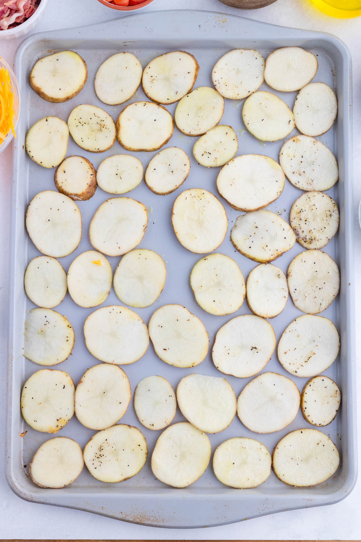Sliced potatoes arranged in a single layer on a baking sheet, lightly seasoned with salt and pepper.