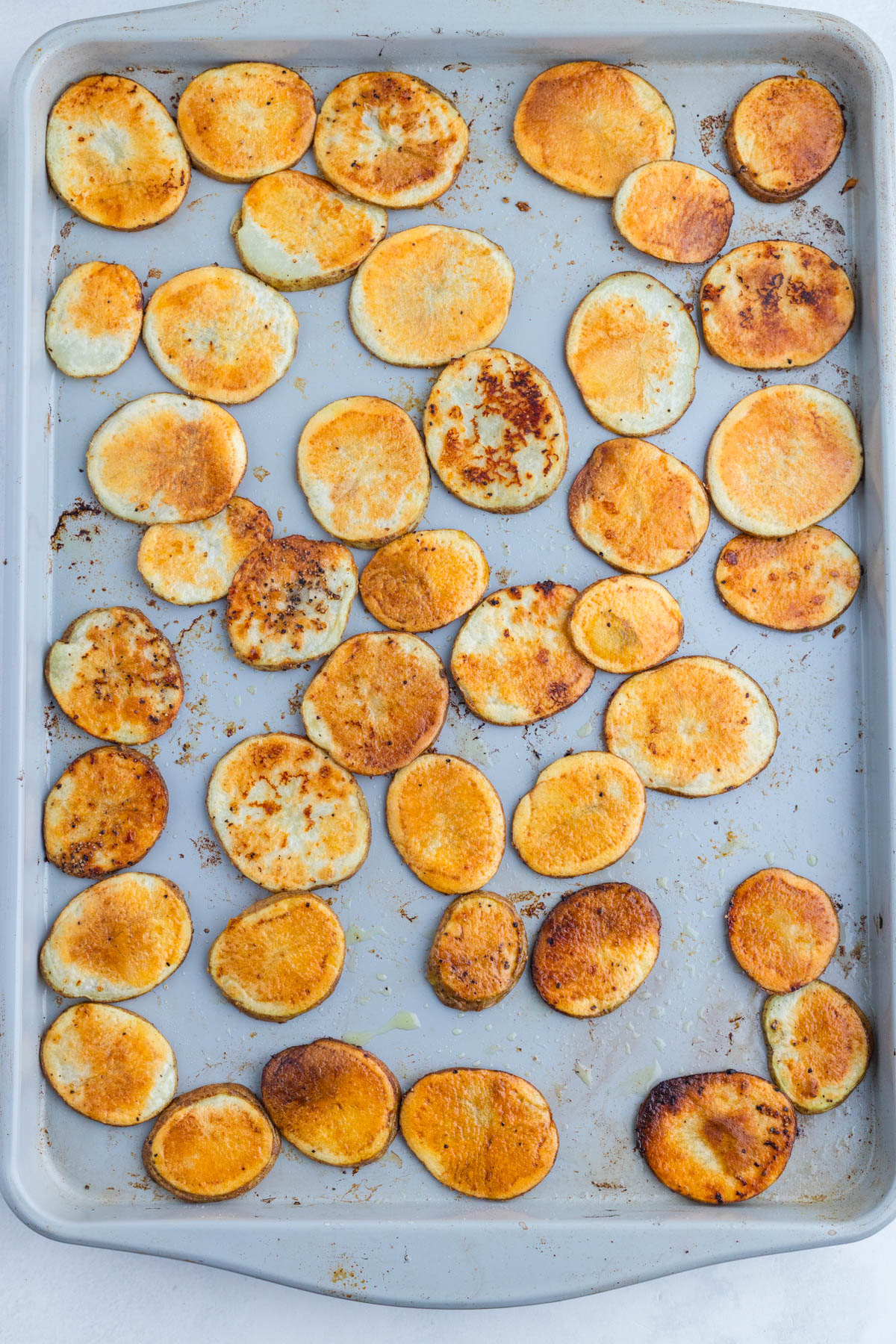 A baking sheet with evenly spaced, round slices of roasted sweet potatoes, showing a golden-brown, slightly crispy surface.