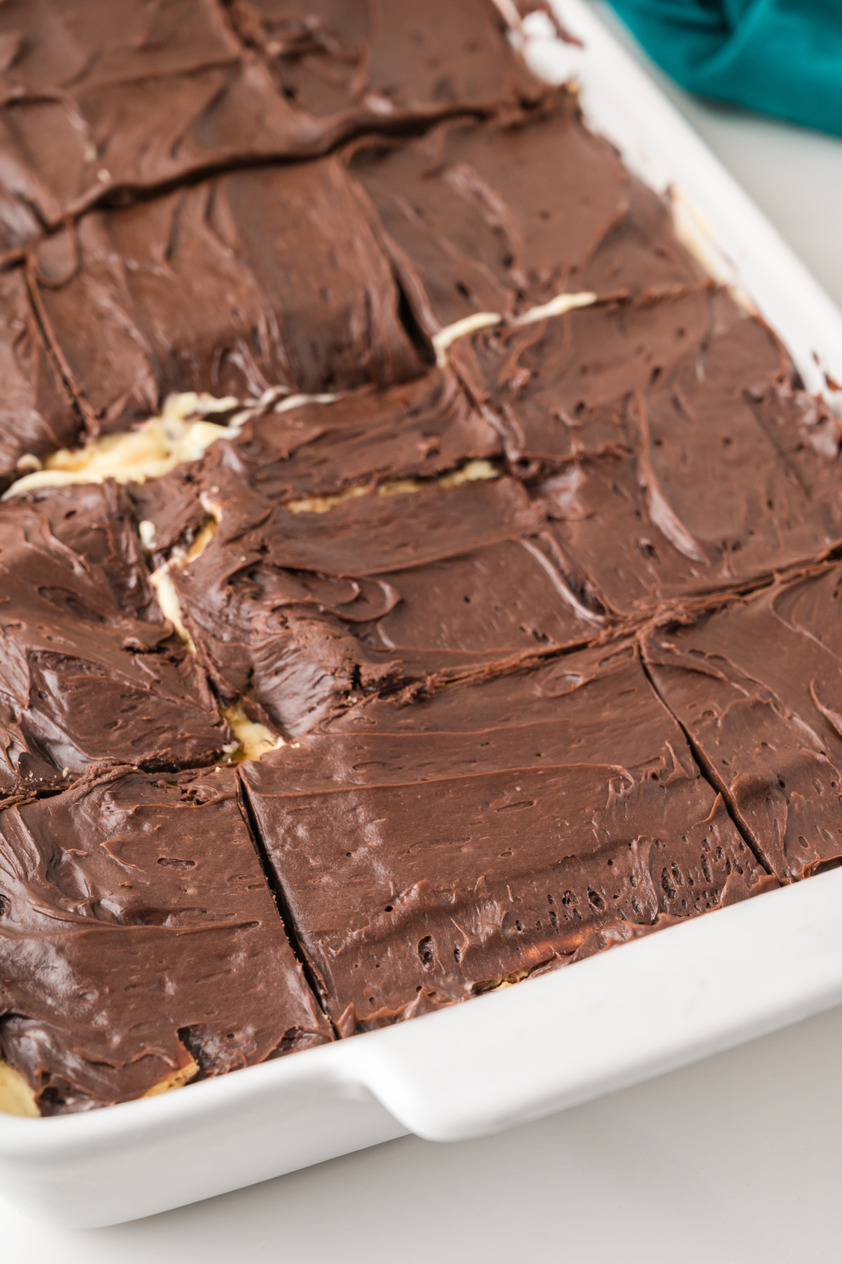 A rectangular dish filled with bars topped with a thick layer of chocolate frosting, cut into squares.