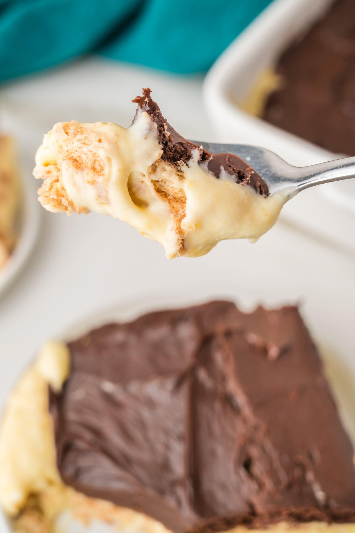 A close-up of a fork holding a bite of dessert with layers of creamy pudding, chocolate topping, and a cookie or cracker crust.